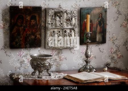 Un vecchio tavolo di preghiera. Vista di un libro e di un candelabro su un tavolo in una camera con interni vintage. Icone vintage sul muro. Angolo accogliente per Praye Foto Stock