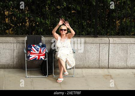 Londra, Regno Unito. 29 giugno 2024. Una donna con una borsa a bandiera del Regno Unito a vita siede su sedie portatili e onde ai carri allegorici durante la sfilata al London Pride 2024. Crediti: Liam Asman/Alamy Live News Foto Stock