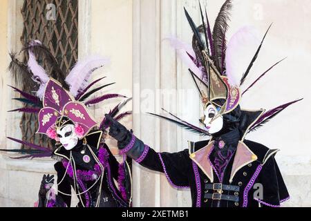 Carnevale di Venezia, coppia in viola con elaborate maschere facciali in posa a Palazzo dei Dogi, Venezia, Veneto, Italia Foto Stock