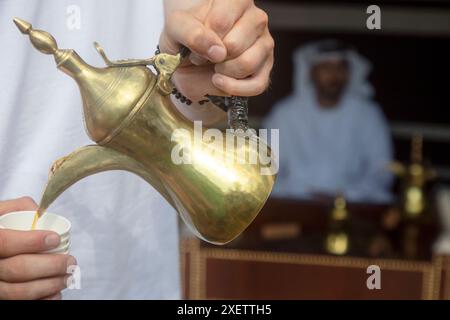 Un uomo versa caffè arabo in una tazza da una tradizionale caffettiera araba Foto Stock