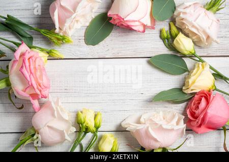 Cornice floreale su sfondo bianco in legno. Eustoma cremoso, eucalipto e rose rosa. Foto Stock