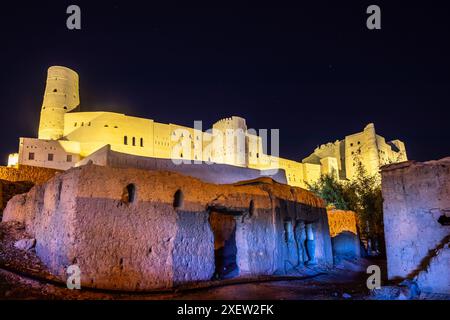 Fortezza di Bahla, mura di pietra e torri rotonde con vecchio edificio in primo piano illuminato di notte, Bahla, Oman Foto Stock