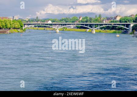 Città di Basilea - Un ponte attraversa il fiume Reno con una città sullo sfondo. Il ponte è una struttura in pietra con un cartello rosso e bianco su di esso. La città è fil Foto Stock