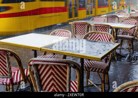 Un treno passa accanto a un ristorante con tavoli e sedie all'esterno. Le sedie sono rosse e gialle e i tavoli sono coperti da panni rossi e bianchi Foto Stock