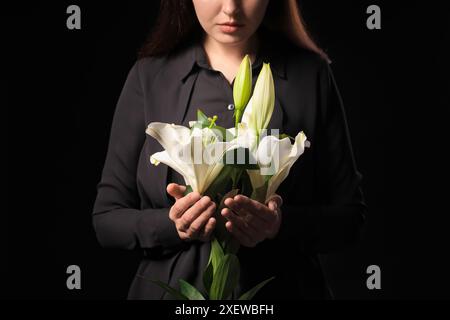Giovane donna con bouquet funebre di fiori di giglio su sfondo nero, primo piano Foto Stock