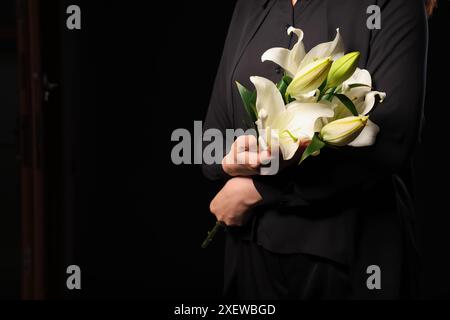 Giovane donna con bouquet funebre di fiori di giglio su sfondo nero, primo piano Foto Stock