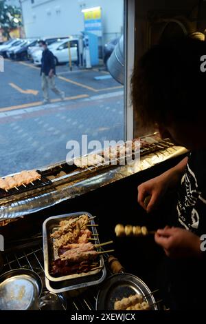 Un giovane giapponese che grigia spiedini al ristorante Washio Yakitori Izakaya a Chuocho, Kagoshima, Giappone. Foto Stock