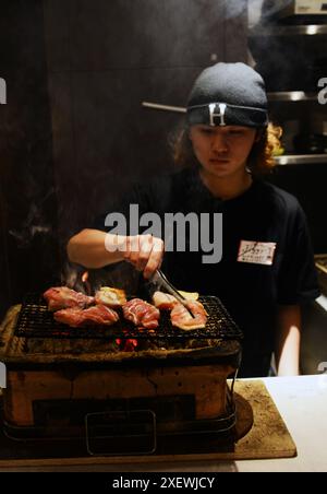 Un giovane giapponese che grigia spiedini al ristorante Washio Yakitori Izakaya a Chuocho, Kagoshima, Giappone. Foto Stock