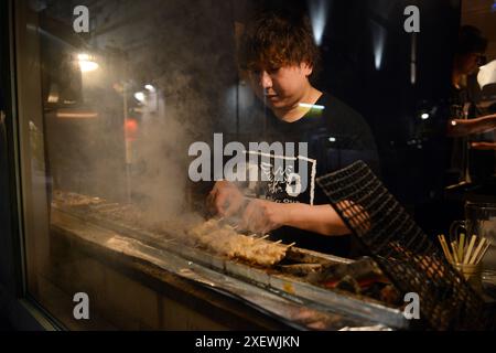 Un giovane giapponese che grigia spiedini al ristorante Washio Yakitori Izakaya a Chuocho, Kagoshima, Giappone. Foto Stock