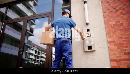 Corriere professionale che utilizza un sistema interfono avanzato per consegne sicure all'ingresso dell'edificio, garantendo la consegna dei pacchi con verifica dell'identità Foto Stock