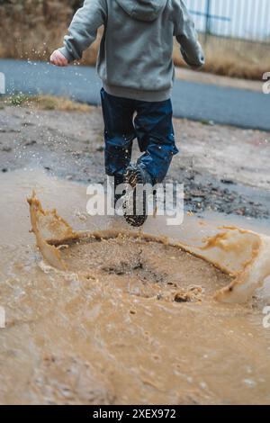 Un ragazzo sta correndo attraverso una pozza d'acqua, spruzzandola ovunque. La scena è divertente e divertente, mentre il ragazzo si diverte sotto la pioggia Foto Stock