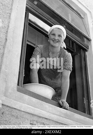 Negli anni '1930 c'era molta gente che puliva Una giovane donna è raffigurata in piedi in una finestra aperta che pulisce e pulisce. 1935 Foto Stock