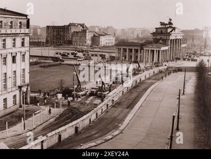 Foto d'epoca della crisi di Berlino del 1961: Costruzione del muro di Berlino rinforzato. Sotto l'occhio vigile della polizia comunista, i lavoratori della Germania Est vicino alla porta di Brandeburgo rafforzano il muro che divide la città. Dopo aver eretto il muro il 13 agosto 1961, per fermare il flusso dei tedeschi dell'Est a Berlino Ovest, i comunisti della Germania Est hanno aggiunto bunker, riflettori e postazioni di fuoco e osservazione. Ottobre 1961 Foto Stock