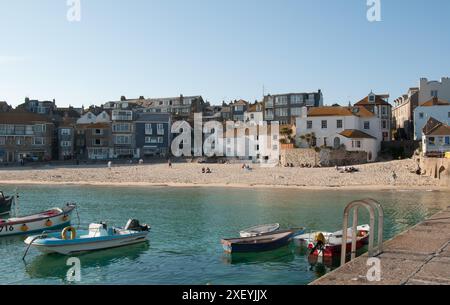 Harbour, St Ives, Cornovaglia, Regno Unito - case che costeggiano il porto in cui sono ormeggiate diverse barche. Piccola spiaggia di fronte a diverse case. Persone in ballo Foto Stock