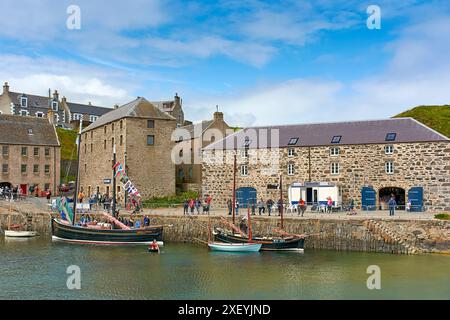 Portsoy Boat Festival piccole barche addobbate con bandiere ormeggiate all'interno del vecchio porto e una ragazza in un coracle Foto Stock