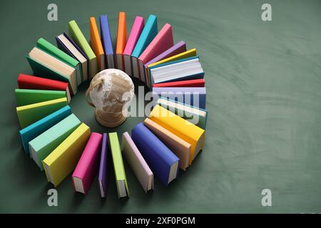 Globo circondato da molti libri colorati su sfondo verde. Spazio per il testo Foto Stock