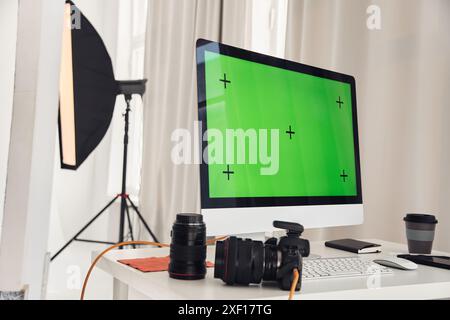 Immagine di sfondo del computer PC con schermo verde in studio fotografico con fotocamere e apparecchiature su un tavolo bianco, spazio di copia Foto Stock