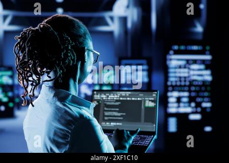 Scienziato informatico che esegue codice e programmazione su laptop, risoluzione dei problemi e aggiornamento di strutture high tech progettate per ospitare più cluster di sistemi server completamente operativi Foto Stock