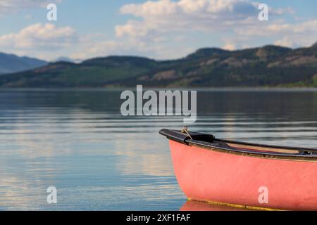 Vista estiva nel nord del Canada con vista sul lago e sulle montagne. Canoa rossa in vista a fuoco. Foto Stock