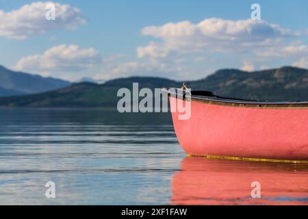 Vista estiva nel nord del Canada con vista sul lago e sulle montagne. Canoa rossa in vista a fuoco. Foto Stock