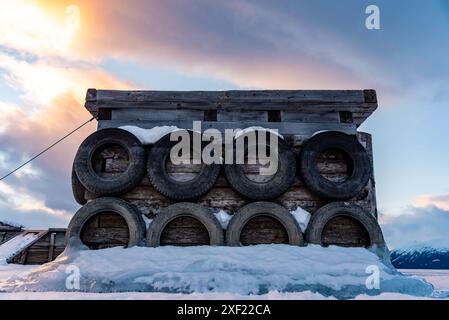 Grandi blocchi di ghiaccio ghiacciati su un porticciolo con pneumatici per auto in inverno. Il tramonto dorato si illumina sul lato di un lago gelido in inverno con il tramonto sullo sfondo. Foto Stock