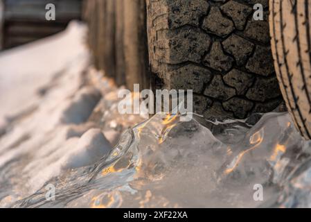 Grandi blocchi di ghiaccio ghiacciati su un porticciolo con pneumatici per auto in inverno. Il tramonto dorato si illumina sul lato di un lago gelido in inverno con il tramonto sullo sfondo. Foto Stock