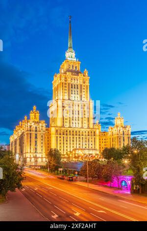 Alto edificio stalinista illuminato vicino al fiume nella notte d'estate a Mosca, Russia. Il nome storico è Hotel Ukraina. Traduzione dell'iscrizione Foto Stock