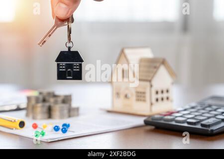 Primo piano di una donna che tiene la chiave di casa in una nuova casa. Agente immobiliare che consegna le chiavi della casa in mano. Un contratto immobiliare, chiavi e una casa in miniatura Foto Stock