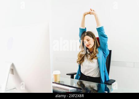 Donna d'affari che si allunga e fa una pausa alla sua scrivania - lavoratrice in ufficio che pratica tecniche di rilassamento in un ambiente professionale - Well luogo di lavoro Foto Stock