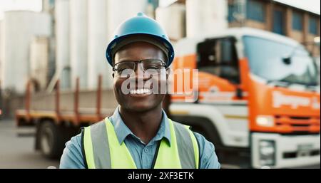 Uomo, ritratto e all'aperto in magazzino con sorriso per logistica, attrezzatura o sicurezza per la salute. Autista maschile, felicità e fabbrica esterna con semi-camion Foto Stock