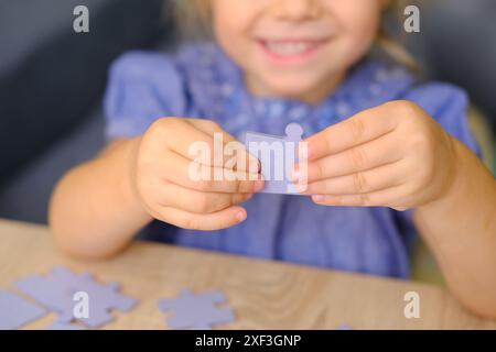 Ragazza allegra e funky di 3 anni che assembla rompicapo, ordina pezzi di cartone per forma, giocattoli educativi e giochi, sviluppo cognitivo del bambino attraverso Foto Stock