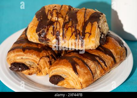 Tre grandi Pain au Chocolates o Pain au Chocolat serviti su un piatto a un tavolo. Una famosa pasticceria francese servita a colazione Foto Stock