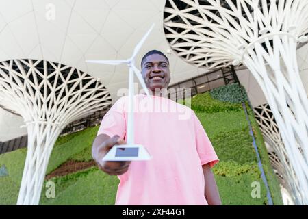 Un uomo con una camicia rosa regge un modello di turbina eolica Foto Stock