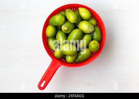 Limoni verdi freschi in cestello rosso di plastica su sfondo di legno chiaro. Vista dall'alto. Foto Stock