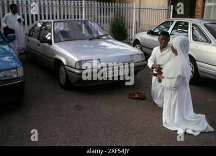 La Fratellanza della Croce e della Stella, questa chiesa semi-cristiana nigeriana fu fondata da Olumba Olumba Obu, noto ai suoi seguaci come OOO. I suoi membri adorano lui e Cristo. Crede di essere l'ottava e ultima reincarnazione del Godhead. Due membri pregano e stringono la mano nel parcheggio della chiesa prima di lasciare la chiesa per la giornata. Elephant and Castle, South London, Inghilterra, anni '1993 1990 UK HOMER SYKES Foto Stock