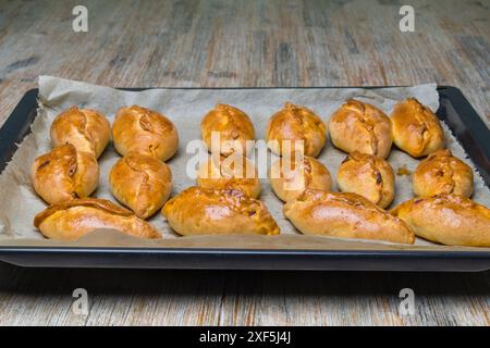 Mini torte Pirozhki o piroshki su un vassoio da cucina Panini a forma di barca con lievito al forno e ripieni di cavolo. Cibo dell'Europa orientale. Foto Stock