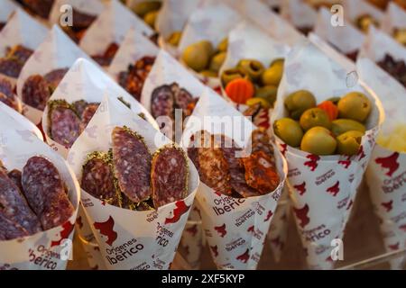 Siviglia, Spagna. 7 febbraio 2024 - salame e olive spagnole venduti in coni di carta in un mercato di siviglia Foto Stock