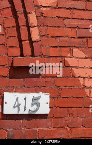 415 su una lavagna bianca contro un edificio vintage in mattoni rossi con arco Foto Stock