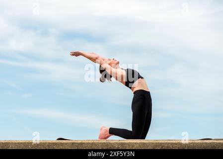 Donna sportiva che si inginocchia facendo un esercizio di backbend, yoga all'aperto Foto Stock