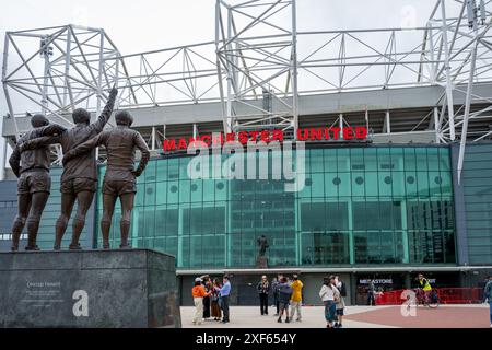 Manchester Trafford Regno Unito 29 giugno 2024. I turisti si riuniscono intorno alla statua della Trinità Unita fuori dal famoso stadio di calcio in una giornata nuvolosa. Foto Stock