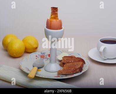 Uovo bollito in parte con soldati toast e una tazza di caffè sullo sfondo. Foto Stock