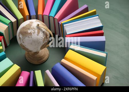 Globo circondato da molti libri colorati su sfondo verde, primo piano Foto Stock
