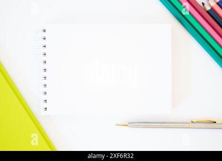 Modello. Vista dall'alto di un foglio bianco di blocco note con campo di immissione su sfondo bianco con matite, penna e cartella. Immagine luminosa. Concetto di business. Educ Foto Stock