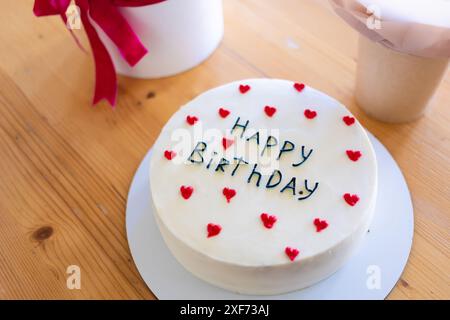 Torta di compleanno con le parole Happy Birthday scritte sopra, circondata da decorazioni a cuore rosso. Foto Stock