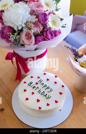 Torta di compleanno con le parole Happy Birthday scritte sopra, circondata da decorazioni a cuore rosso. Foto Stock