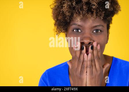 Una donna con i capelli scuri e una camicia blu si sta coprendo la bocca con la mano Foto Stock