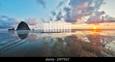 USA, Oregon, Cannon Beach. Colori dorati del tramonto con increspature sulla spiaggia sabbiosa e sulla roccia di Haystack Foto Stock