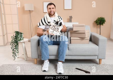 Giovane felice con scarpe nuove e laptop sul divano di casa Foto Stock