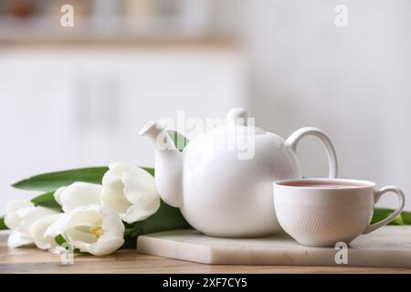 Teiera e tazza vicino ai tulipani sul tavolo su sfondo sfocato Foto Stock