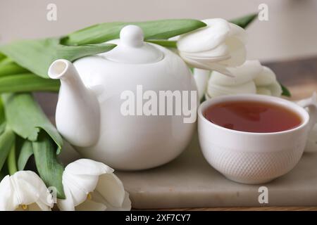 Teiera e tazza vicino ai tulipani sul tavolo su sfondo sfocato Foto Stock
